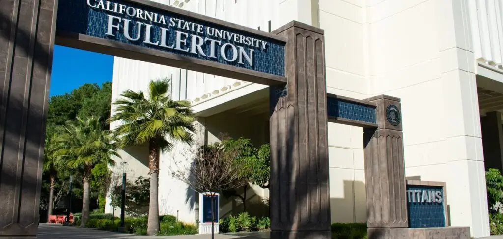 The main entrance of California State University, Fullerton, featuring an iconic archway with the university's name, surrounded by tall palm trees and lush greenery. The modern architectural design of the archway complements the campus buildings, creating a welcoming and vibrant atmosphere.